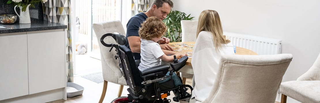 Boy in wheelchair playing a game with his parents.